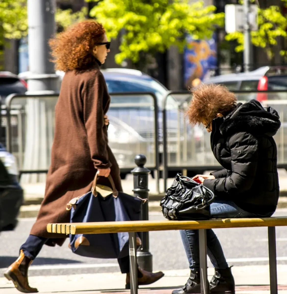 Seated woman checking her bag while another woman walks past